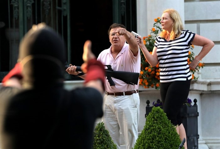 FILE - In this June 28, 2020 file photo, armed homeowners Mark and Patricia McCloskey, standing in front their house along Portland Place confront protesters marching to St. Louis Mayor Lyda Krewson's house in the Central West End of St. Louis. St. Louis’ top prosecutor told The Associated Press on Monday, July 20, 2020 that she is charging a white husband and wife with felony unlawful use of a weapon for displaying guns during a racial injustice protest outside their mansion. 