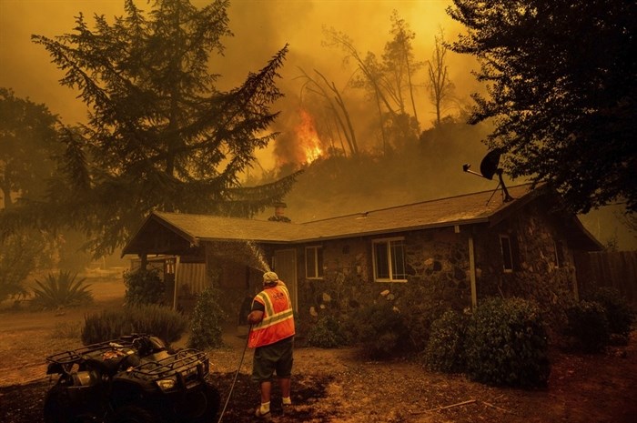 FILE - In this Aug. 18, 2020, file photo, Jerry Kuny sprays water on a home as flames from the LNU Lightning Complex fires approach in unincorporated Napa County, Calif. This home remained standing as the main front passed although the fire went on to destroy multiple residences.