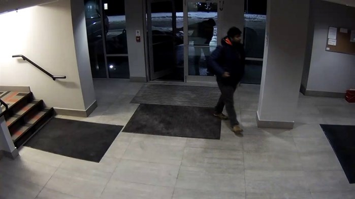 The second unknown man is described as; dark skinned, with dark hair and facial hair, wearing a dark coloured (possibly blue) winter jacket, with an orange lined hood and a dark coloured backpack. This man is seen in the photo entering the lobby through the glass doors.