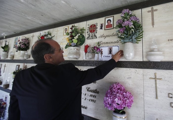 Priest Mario Carminati touches a picture of his nephew Christian Persico, who died from symptoms of coronavirus, at a cemetery in Casnigo, near Bergamo, Italy, Sunday, Sept. 27, 2020. “This thing should make us all reflect. The problem is that we think we’re all immortal,” the priest said.