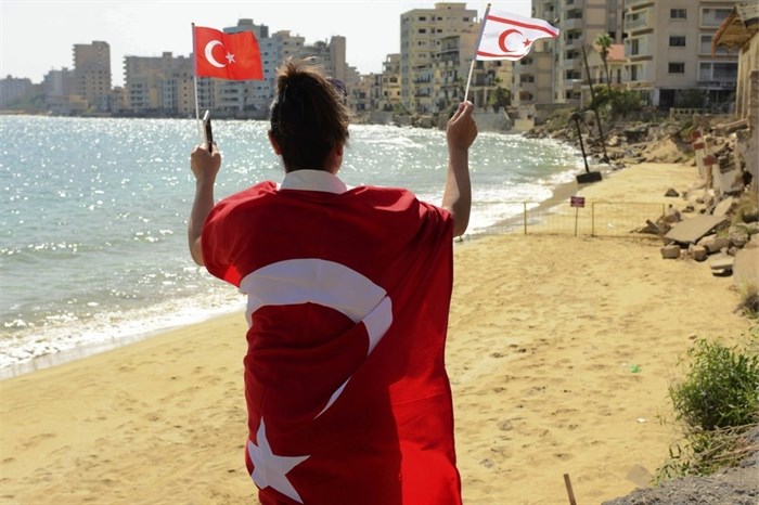 A woman with Turkish and Turkish Cypriot breakaway flags walks along at the beach with abandoned hotels after police open the beachfront of Varosha, an uninhabited, fenced-off suburb in war-divided Cyprus' in the Turkish occupied area in the breakaway Turkish Cypriot north on Thursday, Oct. 8, 2020. The United Nations and the European Union have expressed concern that Turkey's move to open the beachfront could hinder renewed efforts to reunify the island, split in 1974 when Turkey invaded following a coup by supporters of union with Greece. 