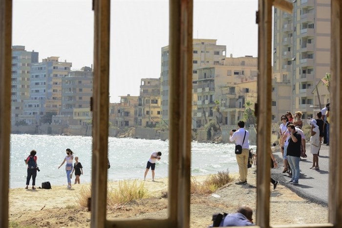 Journalists and public are seen through a window frame at the beach with abandoned hotels, after police open the beachfront of Varosha, an uninhabited, fenced-off suburb in war-divided Cyprus' in the Turkish occupied area in the breakaway Turkish Cypriot north on Thursday, Oct. 8, 2020. The United Nations and the European Union have expressed concern that Turkey's move to open the beachfront could hinder renewed efforts to reunify the island, split in 1974 when Turkey invaded following a coup by supporters of union with Greece.