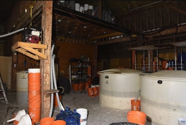 Workshop interior strewn with buckets, chemical containers and large white plastic holding tanks.