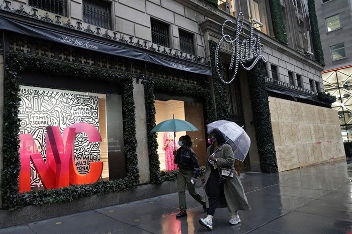 People walk past a partially-boarded up Saks Fifth Avenue, Sunday, Nov. 1, 2020, in New York. Retailers including Nordstrom, Tiffany and Saks are planning to board up their windows or add extra security personnel in some of their locations ahead of the contentious presidential election on Tuesday. 