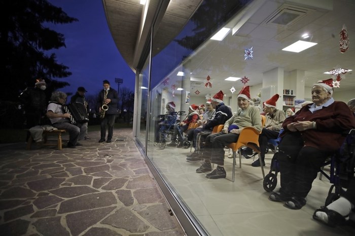 FILE - In this Dec. 19, 2020, file photo, hosts, protected by glass window, attend a Christmas concert in a nursing home in Alzano Lombardo, one of the area that most suffered the first wave of COVID-19, in Northern Italy. All most people wanted for Christmas after this year of pandemic was some cheer and togetherness. Instead many are heading into a season of isolation, grieving lost loved ones, experiencing uncertainty about their jobs or confronting the fear of a potentially more contagious variant of the coronavirus.