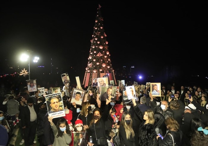 FILE - In this Dec. 21, 2020, file photo, relatives of victims killed during the Beirut port explosion hold up their portraits as they stand near a Christmas tree decorated with their names during a Christmas event to commemorate them, in Beirut, Lebanon. While many countries tightened restrictions, Lebanon, with the largest percentage of Christians in the Middle East, was actually easing them despite rapidly growing cases. It made that decision to boost an ailing economy and alleviate despair exacerbated by a devastating port explosion in Beirut in August. 