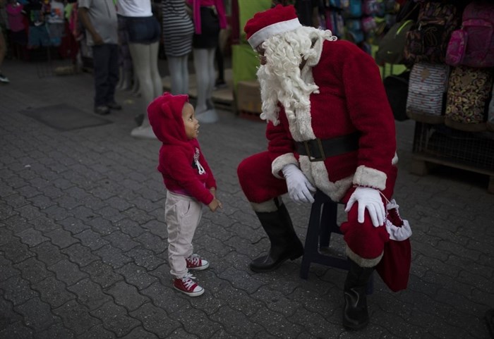 FILE - In this Dec. 18, 2020, file photo, Fredy Parra, dressed as Santa Claus, speaks to a girl at a Christmas fair in Caracas, Venezuela. For more than 10 years, children have had their picture taken with Parra at the fair for a small fee. 