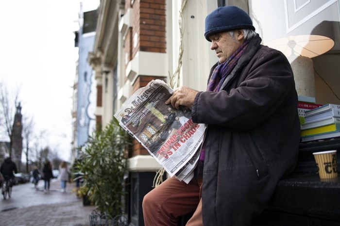 A man turns a page as he reads a newspaper with a headline reading 