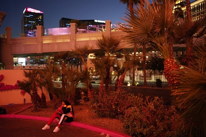 A woman sits on a curb along the Strip in Las Vegas, Feb. 10, 2021. Visitor numbers in Las Vegas were down by more than half in 2020 compared to 2019, according to data compiled by tourism, airport and gambling regulators.