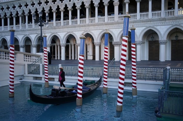 A gondolier stands by a boat near a quiet pedestrian walkway at the Venetian hotel and casino in Las Vegas, Feb. 4, 2021. The toll of the coronavirus is reshaping Las Vegas almost a year after the pandemic took hold. The tourist destination known for bright lights, big crowds, indulgent meals and headline shows is a much quieter place these days. 