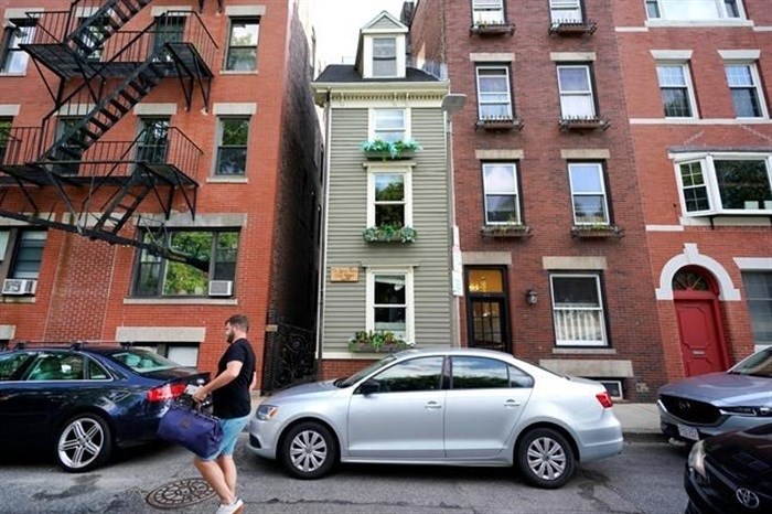 FILE — In this Aug. 13, 2021 file photograph, a man walks by Boston's famous Skinny House, at center, after it was listed for sale for $1.2 million. The sale of the home was closed Thursday Sept. 16, 2021 for $1.25 million, according to Zillow. The home "received multiple offers and went under agreement for over list price in less than one week," real estate agency CL Properties posted on Facebook.