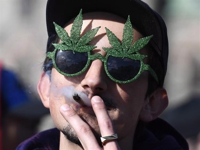 A man smokes a marijuana joint during the annual 4/20 celebration on Parliament Hill in Ottawa, Friday, April 20, 2018. B.C.'s privately-owned cannabis stores can now start stocking pot-themed clothing, books and other goods.