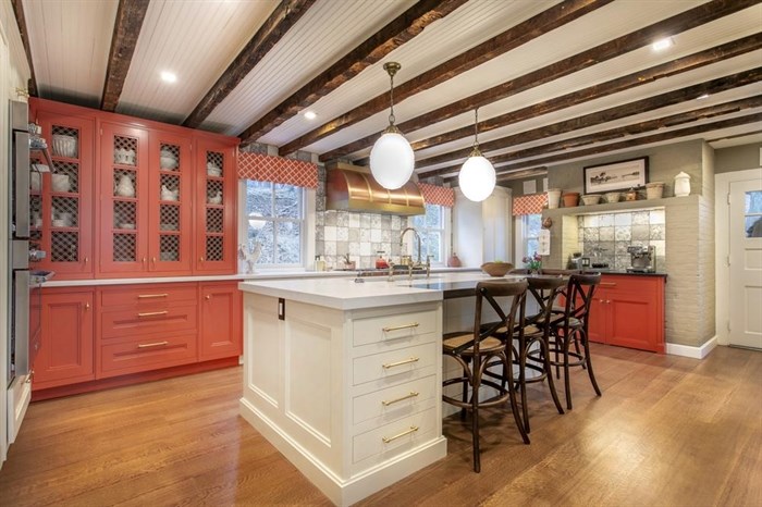 This image released by Bakes & Kropp shows the Cold Spring Harbor kitchen with hutch cabinetry and a coffee bar painted in Benjamin Moore’s fresh, cheerful Geranium, with white Farrow & Ball’s Lime White on the island and perimeter cabinets. Large lighting fixtures, like these from Hudson Lighting, add punctuation to the dramatic yet homey overall design.