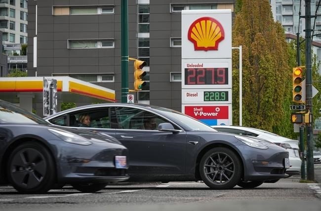 Tesla electric vehicles drive past a sign displaying the price of a litre of regular gasoline after it reached a new high of $2.28 in Vancouver on Saturday, May 14, 2022.