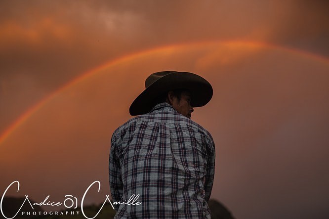 A photo by Candice Camille of her husband Jordan riding a horse named Lucky under a rainbow.
