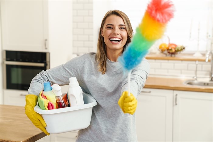 A cleaner holding cleanser bottles and a colourful duster