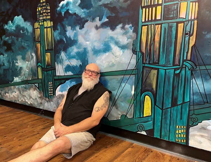 Kamloops business owner David Pup Johnston leaning against a mural by Kamloops based artist Stace DeWolf at Nightshift on Fifth.