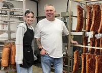 Owner of Gary&#39;s European Sausage and Deli in Kamloops, Jurgen Gemsa (right) stands beside employee Haille Baird next to a rack of smoked bacon. 