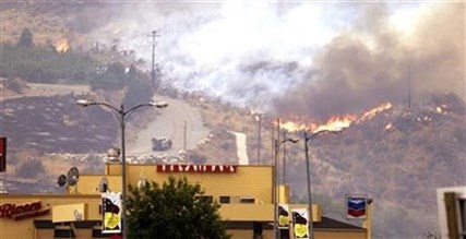 Flames creep down a hillside in view of businesses Friday, July 18, 2014, in Pateros, Wash.