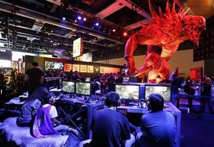 A giant monster looms over gamers playing Evolve, a video game published by 2K Games, Friday, Aug. 29, 2014, at the Penny Arcade Expo in Seattle.