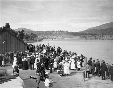 The crowd waiting on the Kelowna wharf as one of the paddlewheelers comes around the point circa 1909.